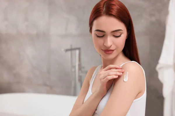 stock image Beautiful young woman applying body cream onto shoulder in bathroom, space for text