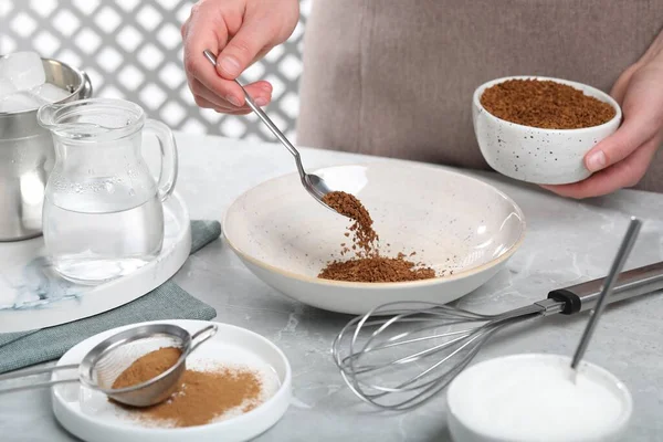煮达戈纳咖啡妇女在浅灰桌旁将速溶颗粒倒入碗中 — 图库照片