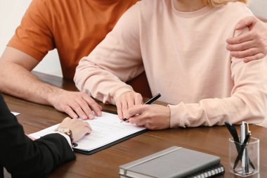 Notary helping couple with paperwork at wooden table, closeup