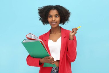 Açık mavi arka planda dosyaları ve kalemi olan Afrikalı Amerikalı stajyer.