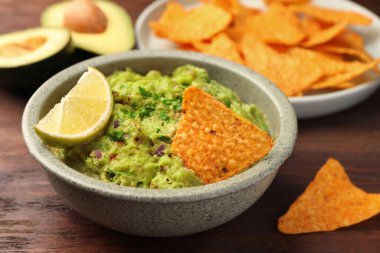 Bir kase lezzetli guacamole, limon ve cips ahşap masada, yakın plan.