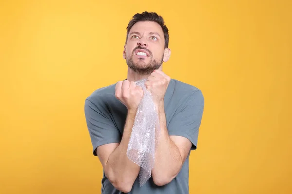 Angry Man Popping Bubble Wrap Yellow Background Stress Relief — Stock Photo, Image