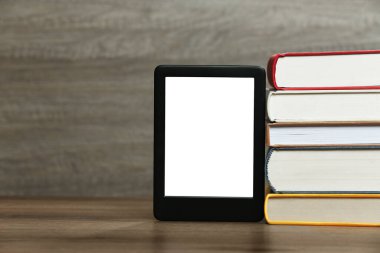 Taşınabilir e-kitap okuyucu ve ahşap masada bir yığın ciltli kitap, metin için yer