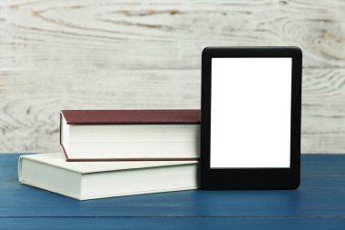 Taşınabilir e-kitap okuyucu ve mavi ahşap masa üzerindeki ciltli kitaplar, metin için alan