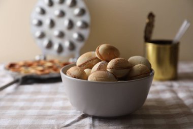 Bir kase lezzetli ceviz şekilli kurabiye ve yoğun sütle damalı masa örtüsü.