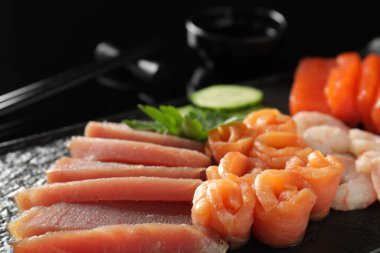 Lezzetli sashimi seti somon, ton balığı ve karides. Siyah servis tahtasında maydanoz ve salatalıkla servis ediliyor.