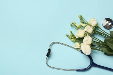 Stetoskop ve açık mavi arkaplanda güzel Eustoma çiçekleri, metin için boş alan. Mutlu Doktor Günleri.
