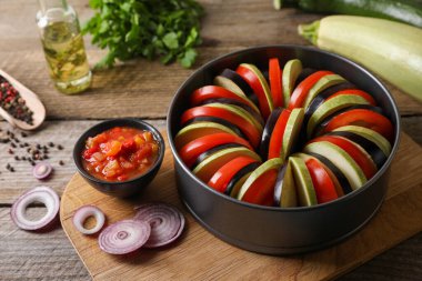 Lezzetli ratatouille pişiriyorum. Farklı taze sebzeler ve ahşap masada yuvarlak pişirme tavası.