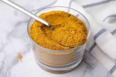 Beyaz mermer masada köri tozu ve kaşık, yakın plan.