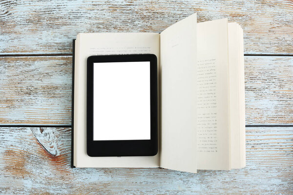 Portable e-book reader and hardcover book on wooden rustic table, top view
