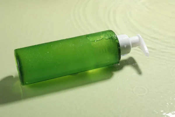 Bottle of facial cleanser in water against olive background
