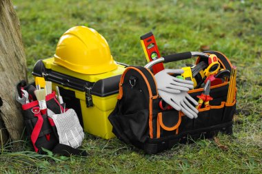 Ağacın yanındaki çimlerin onarılması için farklı aletler içeren çanta, kemer ve kutu.