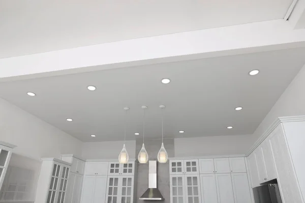 Ceiling with modern lamps, furniture and cooker hood in stylish kitchen, low angle view