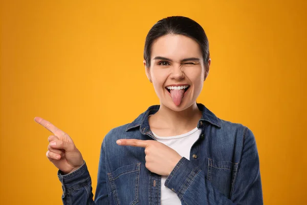 Szczęśliwa Młoda Kobieta Pokazuje Swój Język Wskazuje Żółte Tło — Zdjęcie stockowe