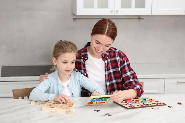 Mutfaktaki beyaz mermer masada farklı matematik oyun setleriyle oynayan mutlu anne ve kız. Matematiği zevkle çalış