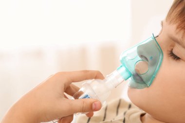 Bulanık arka planda nefes almak için nebulizör kullanan çocuk, yakın plan