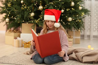 Noel Baba şapkalı şirin bir kız ağacın yanında kitap okuyor ve evde hediyeler veriyor. Noel atmosferi