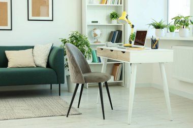 Modern dizüstü bilgisayarı beyaz ahşap masa ve evdeki rahat koltuğu olan rahat çalışma alanı.