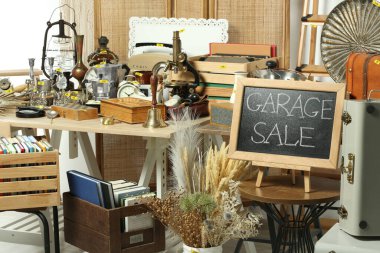 Sign Garage Sale written on blackboard near many different stuff indoors