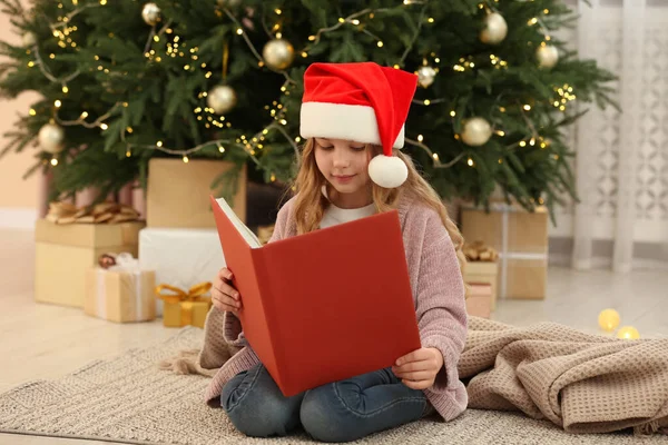 Симпатичная Маленькая Девочка Санта Шляпе Читает Книгу Возле Елки Подарки — стоковое фото