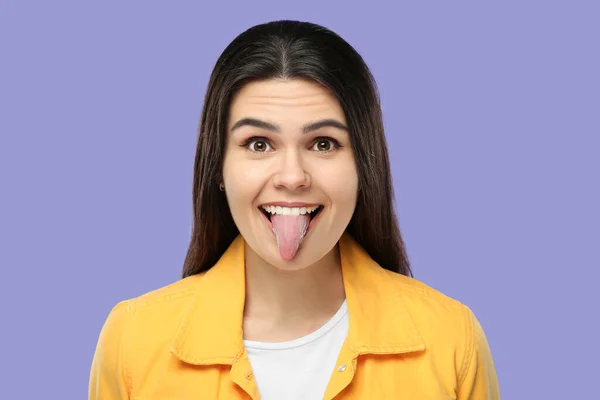快乐的年轻女子 在紫色背景上露出她的舌头 — 图库照片
