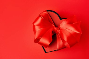 Güzel kalp şeklinde hediye kutusu, kırmızı arka planda fiyonk, üst manzara.