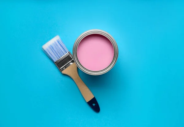 Can with pink paint and brush on light blue background, flat lay