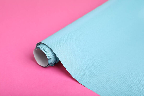 Roll of light blue wrapping paper on pink background, closeup