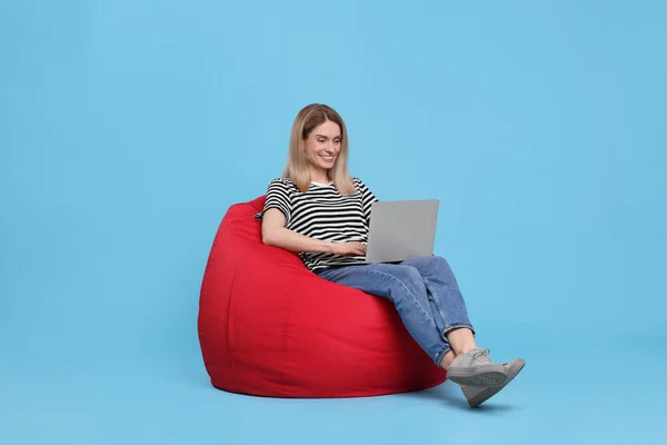 Glückliche Frau Mit Laptop Sitzt Auf Sitzsack Stuhl Vor Hellblauem — Stockfoto