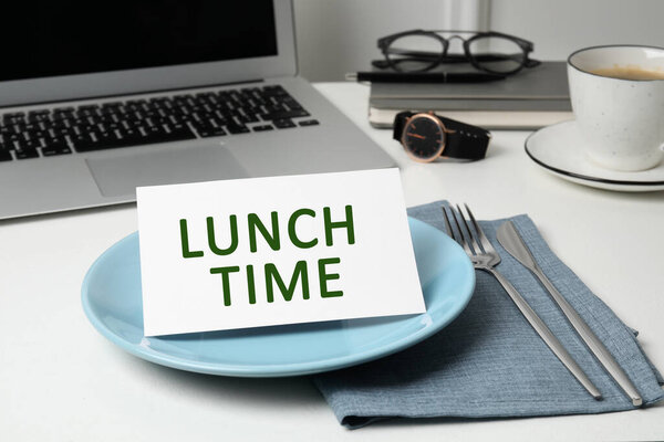Business lunch. Office desk with plate, cutlery and laptop. Card with phrase Lunch Time on dish