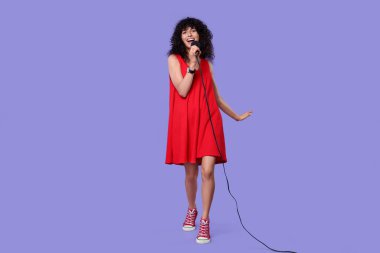 Mor arka planda mikrofonlu güzel genç bir kadın şarkı söylüyor.