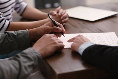 Notary helping couple with paperwork at wooden table, closeup