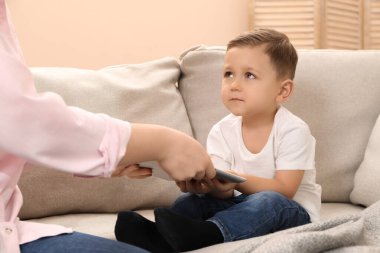 İnternet bağımlılığı. Anne, evdeki kanepede oğlunun tabletini alıp kapatıyor.