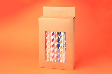 Box with many paper drinking straws on orange background