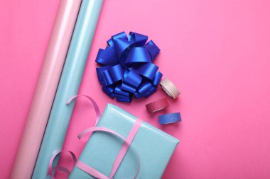 Paket kağıdı ruloları, hediye kutusu, pembe arka planda fiyonk ve kurdeleler.