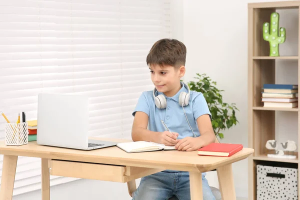 stock image Boy writing in notepad near laptop at desk in room. Home workplace