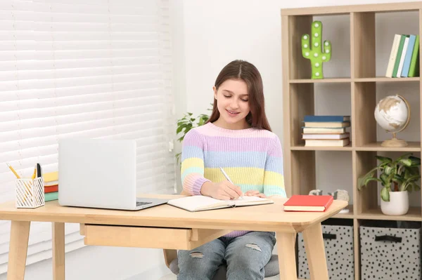 ノートパソコンのそばの机の上に 可愛い女の子がノートを書いています ホームワーク — ストック写真