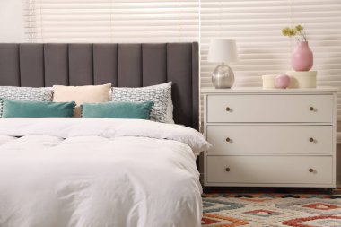 Yastıkları, lambası ve beyaz çekmeceleri olan rahat bir yatak. Şık iç mekan