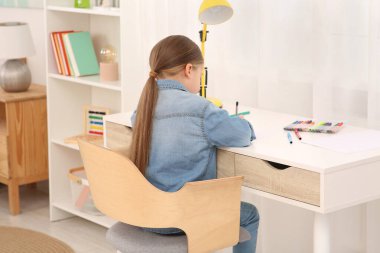 Masasında keçeli kalemler olan şirin küçük bir kız. Ev işyeri