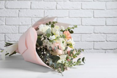 Beyaz tuğla duvara karşı ahşap masada duran bir buket güzel çiçek. Metin için boşluk
