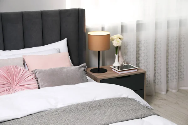 クッション ランプと部屋のベッドサイドテーブルの異なる装飾が施された快適なベッド スタイリッシュなインテリア — ストック写真