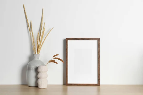 Empty photo frame and vases with dry decorative spikes on wooden table. Mockup for design
