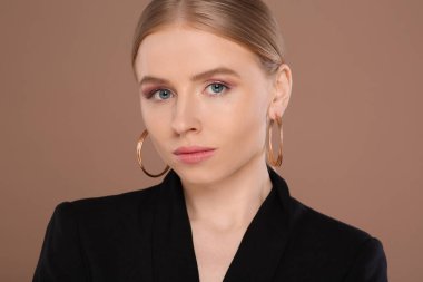 Açık kahverengi arka planda zarif küpeleri olan güzel genç bir kadın.