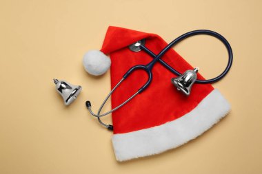 Steteskoplu doktor için tebrik kartı, Noel Baba şapkası ve bej arka planda Noel dekoru, düz yatış