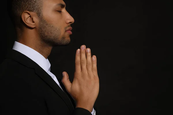 stock image African American man with clasped hands praying to God on black background. Space for text