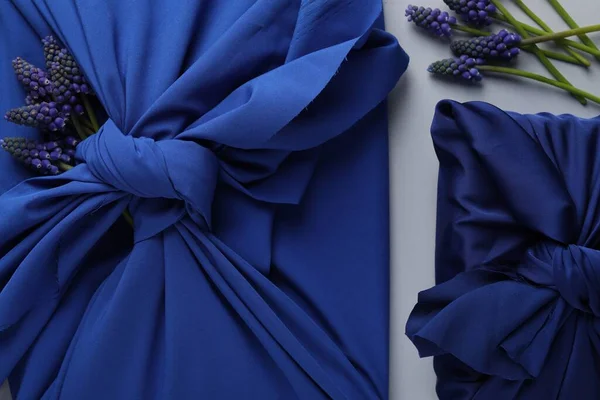 stock image Furoshiki technique. Gifts packed in blue silk fabric and muscari flowers on white table, flat lay