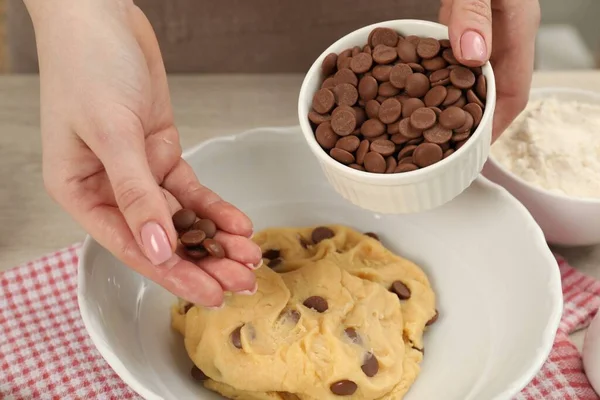 Cooking sweet cookies. Woman adding chocolate chips to dough at table, closeup