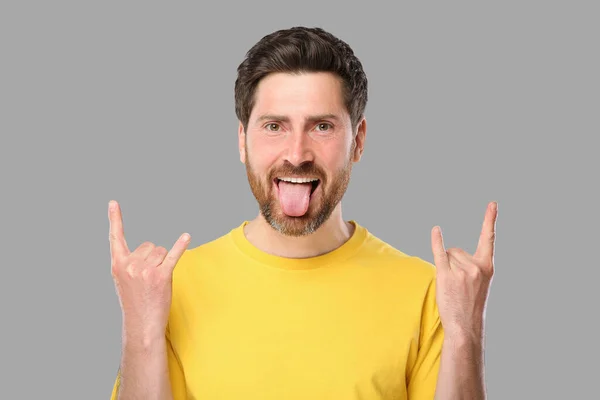Człowiek Pokazuje Swój Język Rock Gest Szarym Tle — Zdjęcie stockowe