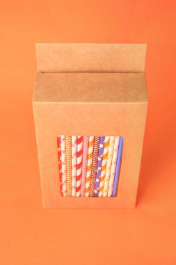 Box with many paper drinking straws on orange background