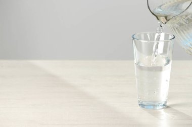 Sürahiden bardağa beyaz masa üzerine su dökülüyor. Metin için boşluk